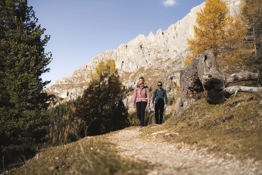 Zwei Frauen wandern auf einem Bergweg vor einer hellen Felswand