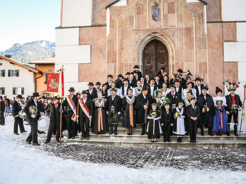 Große Gruppe in traditioneller Tracht vor Kirche im verschneiten Dorf