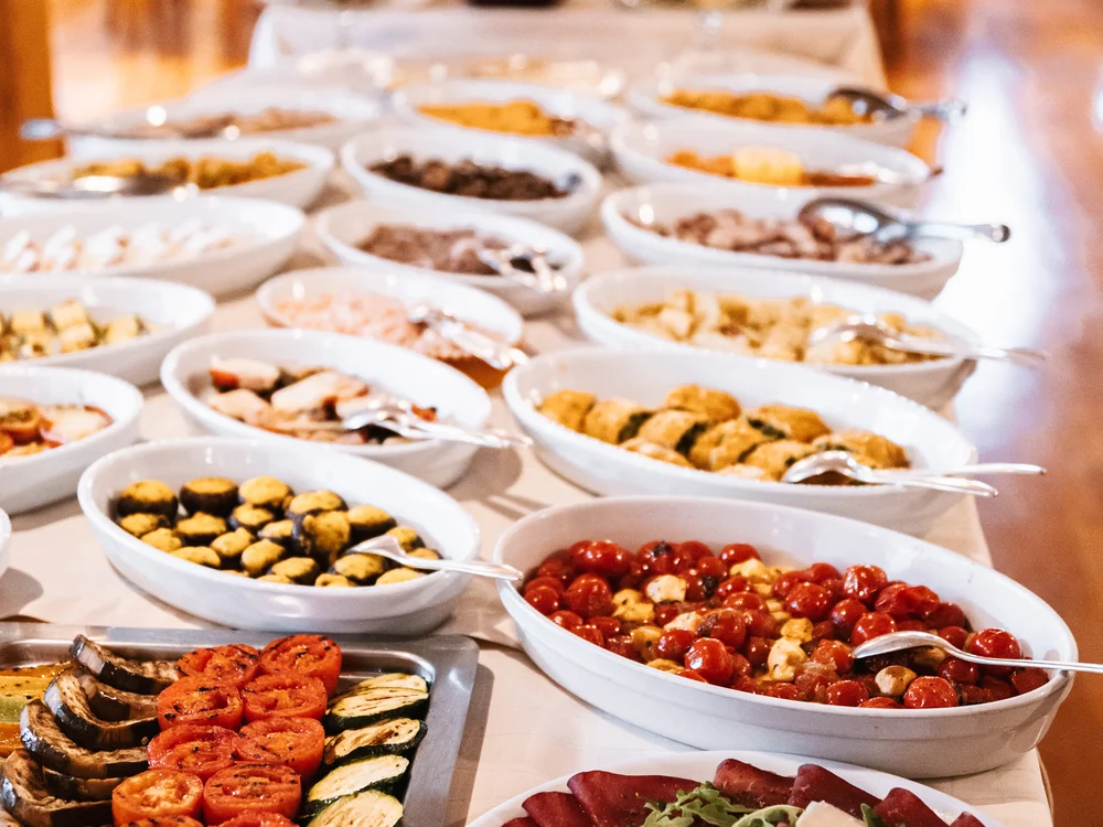 Buffet mit verschiedenen Antipasti und Gemüsescheiben in weißen Schalen