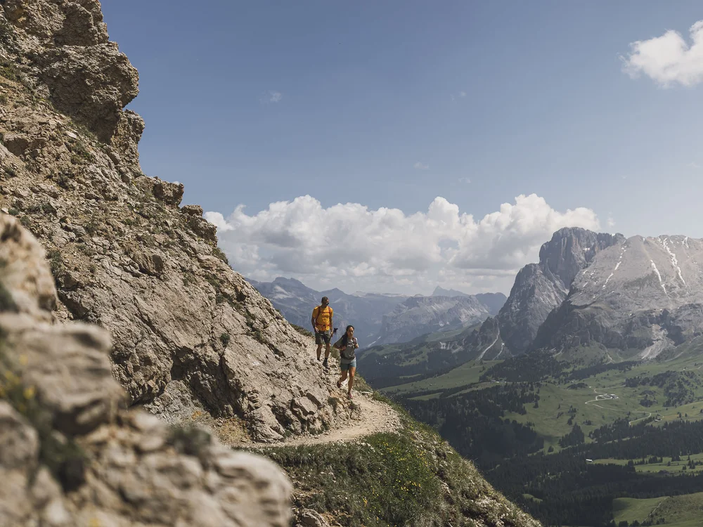 Wanderer auf schmalem Bergpfad mit Felswand und weitem Tal im Hintergrund