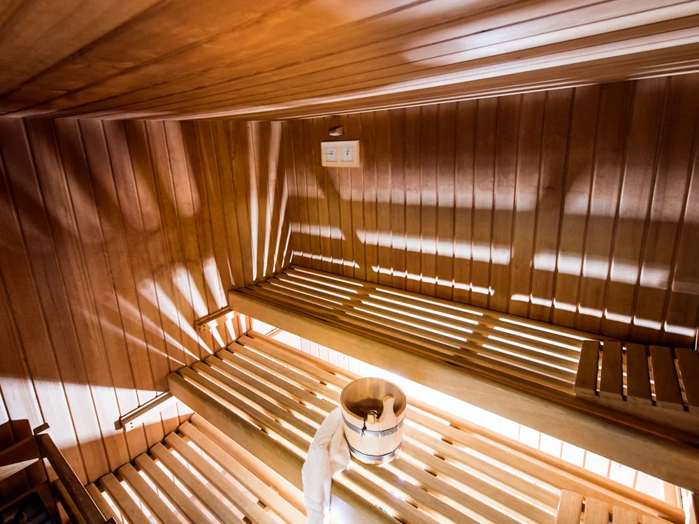 Innenansicht einer holzverkleideten Sauna mit Holzeimer und Handtuch