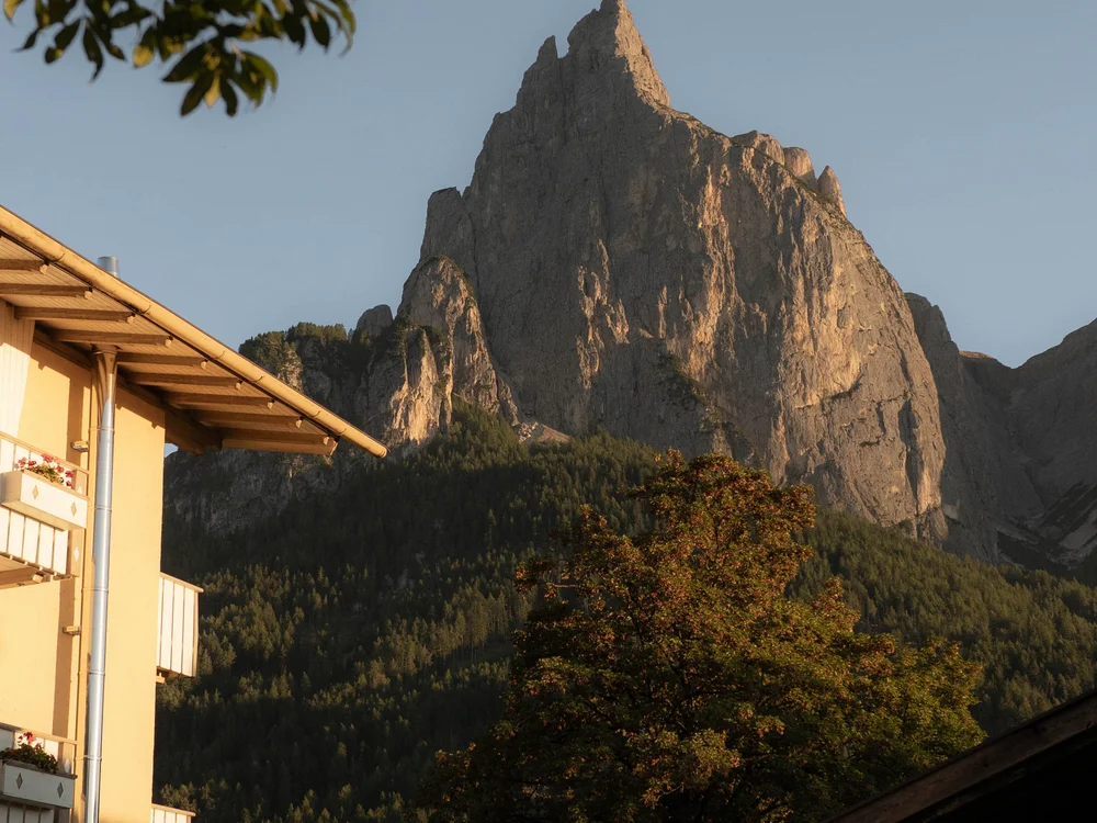 Felsiger Berggipfel mit Häusern und Bäumen im Vordergrund bei klarem Himmel