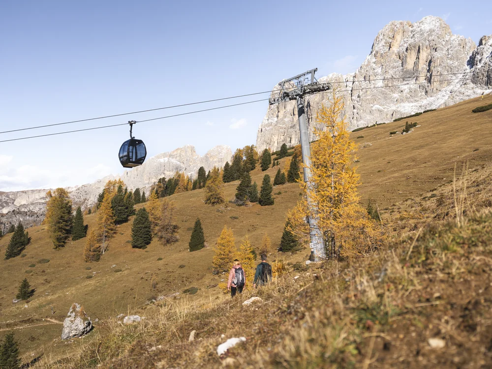 Seilbahn über herbstlicher Berglandschaft mit Wanderern und felsigen Gipfeln
