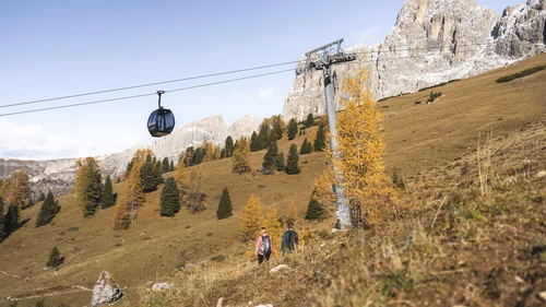 Seilbahn über herbstlicher Berglandschaft mit Wanderern und felsigen Gipfeln