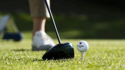 Golfball auf Tee vor Golfschläger auf grünem Rasen