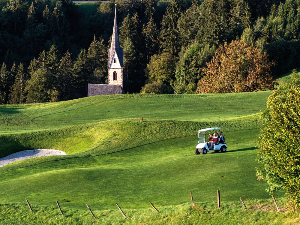 Golfplatz mit Kirchengebäude und Golfwagen in grüner Landschaft