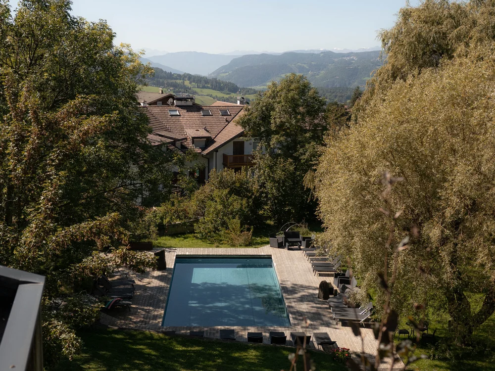 Schwimmbad mit Liegestühlen in einem Garten mit Bäumen und Bergen im Hintergrund