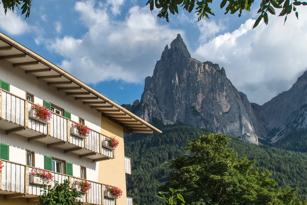 Haus mit Blumenbalkonen vor Berglandschaft und blauem Himmel