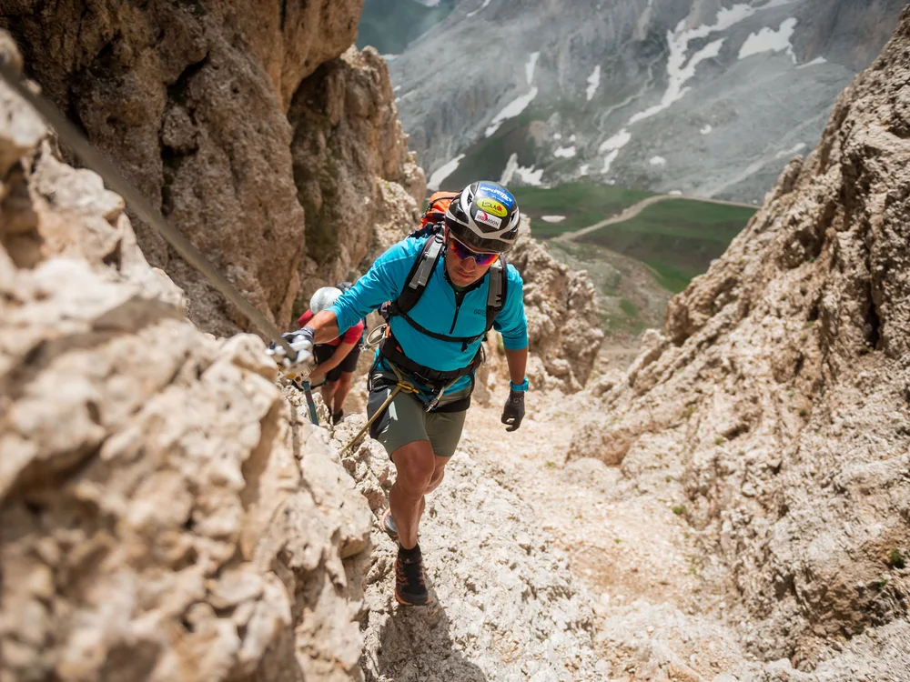 Bergsteiger in blauer Outdoor-Ausrüstung klettert steilen Felsen mit Blick ins Tal