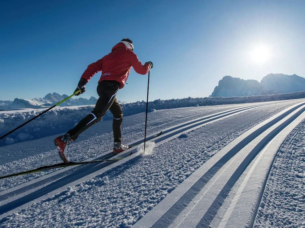 Langläufer in roter Jacke auf präparierter Loipe bei sonnigem Winterwetter