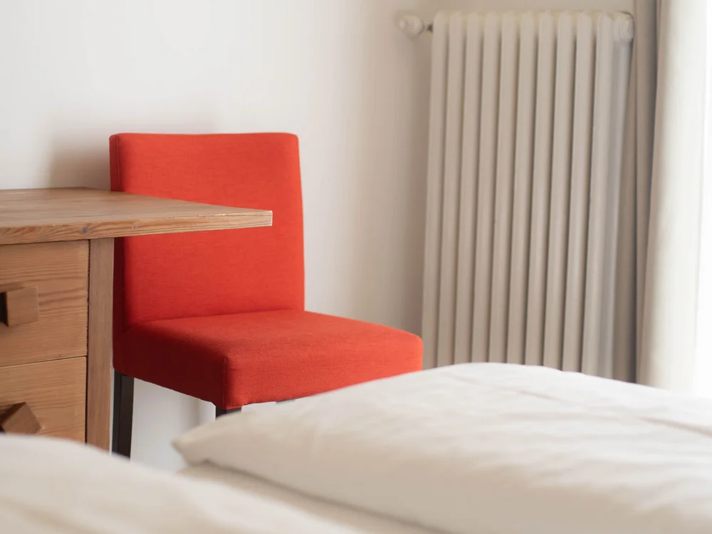 Roter Stuhl neben Holztisch und Bett in hellem Zimmer