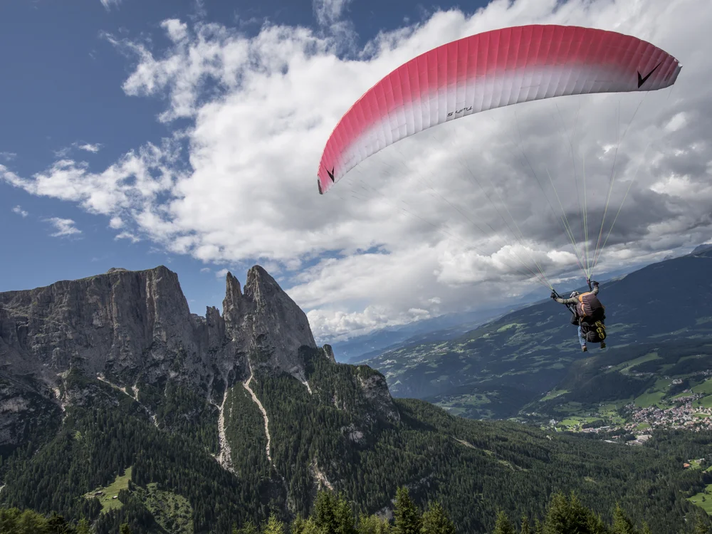 Person beim Gleitschirmfliegen über bewaldeten Bergen und Tal