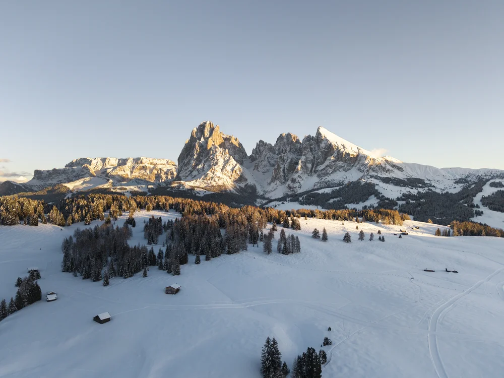 Schneebedeckte Alpenlandschaft mit Bäumen und Hütten bei Sonnenuntergang