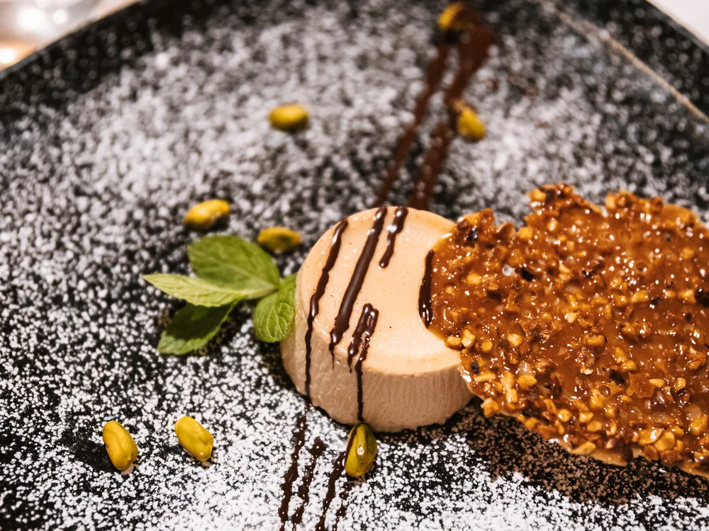 Kunstvoll angerichtetes Dessert mit Karamellcrisp und Minzblatt auf schwarzem Teller