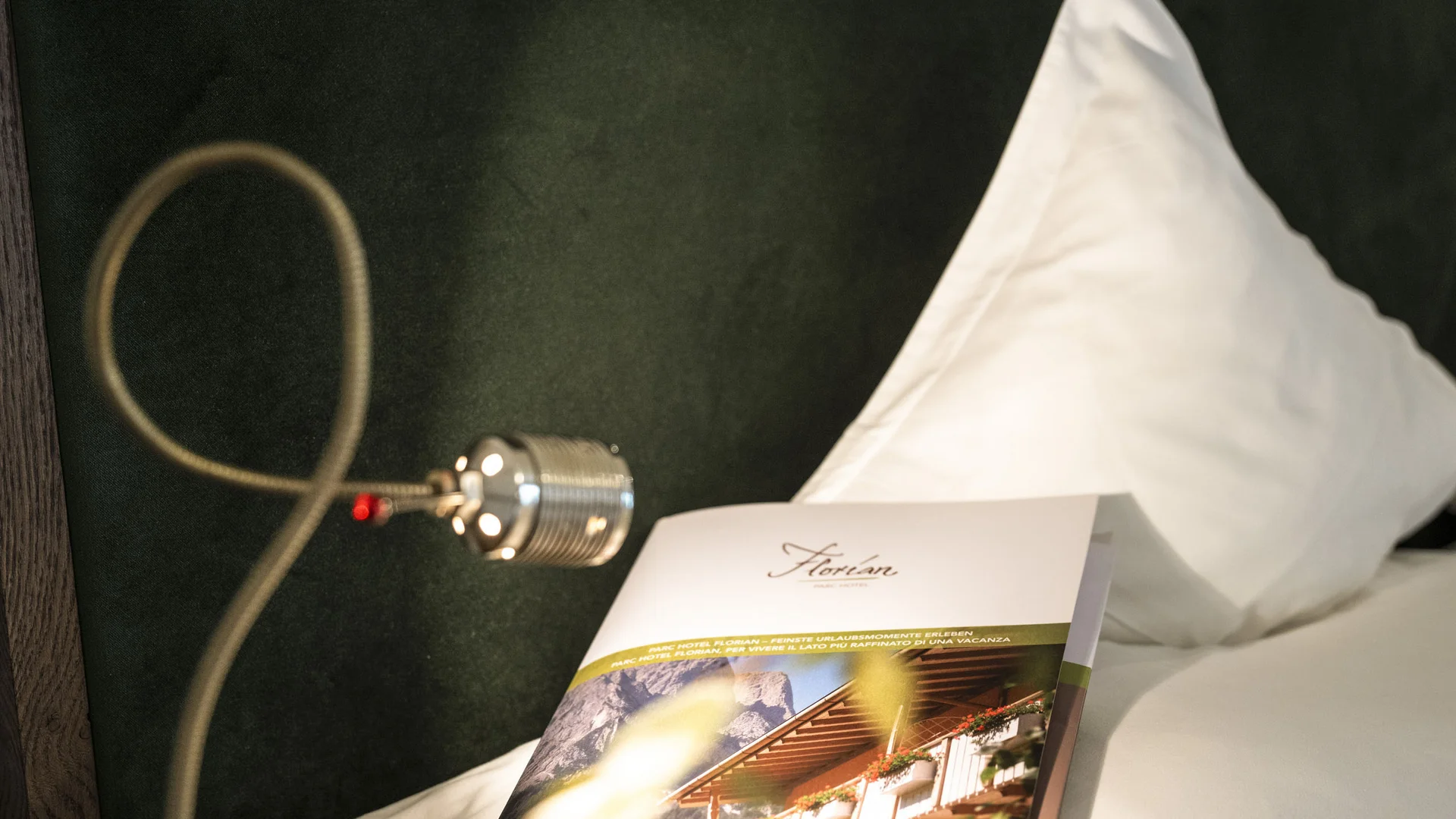Broschüre auf einem Kissen und Wandlampe im Hotelzimmer