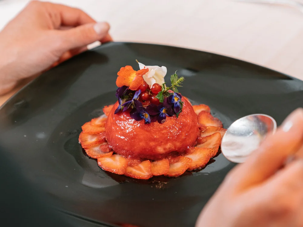 Angerichteter Nachtisch mit Erdbeeren und essbaren Blumen auf dunklem Teller