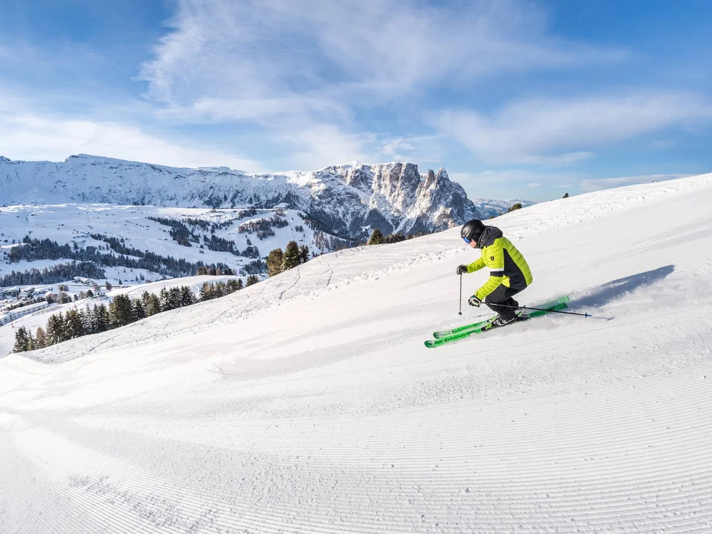 Skifahrer in grüner Jacke fährt auf präparierter Piste mit Bergblick
