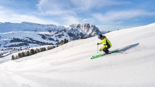 Skifahrer in grüner Jacke fährt auf präparierter Piste mit Bergblick