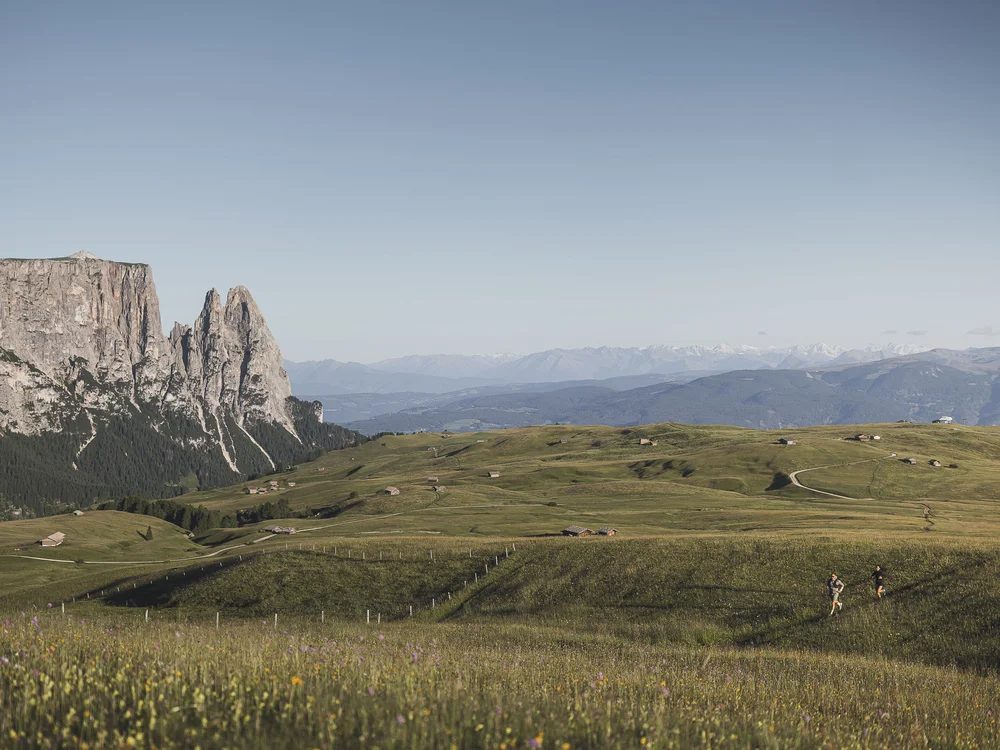 Berglandschaft mit grünen Wiesen und zwei laufenden Menschen im Vordergrund
