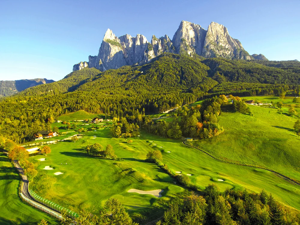 Grünes Tal mit Golfplatz und spitzen Berggipfeln im Hintergrund bei klarem Himmel