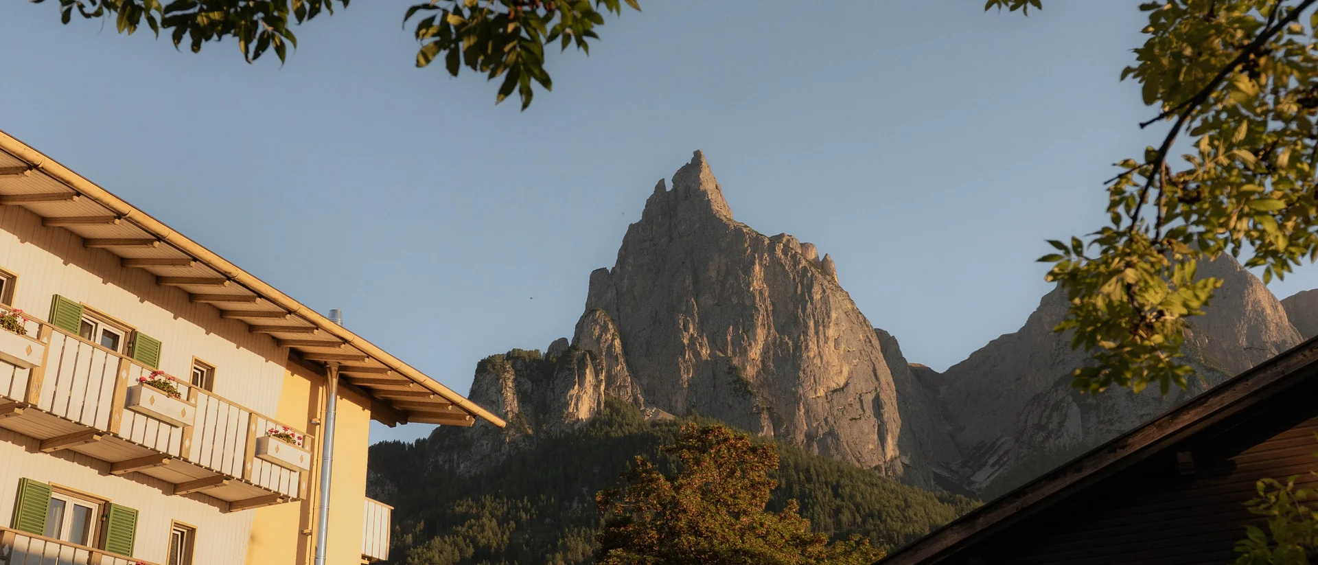 Bergspitze bei Sonnenuntergang mit Häusern und Bäumen im Vordergrund
