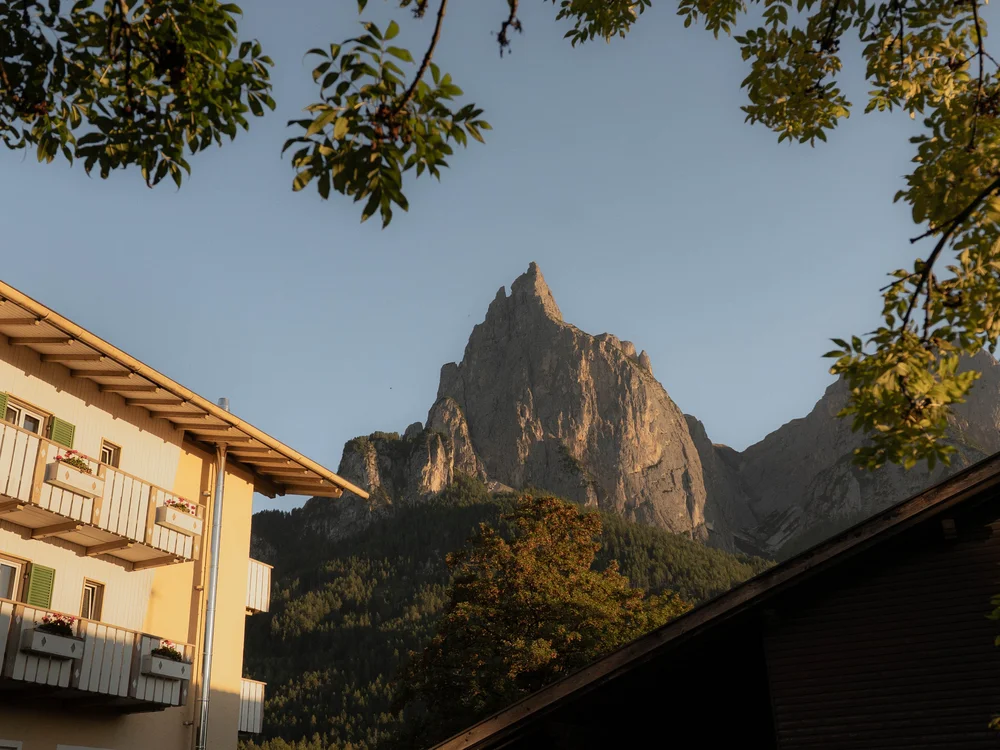 Bergspitze bei Sonnenuntergang mit Häusern und Bäumen im Vordergrund