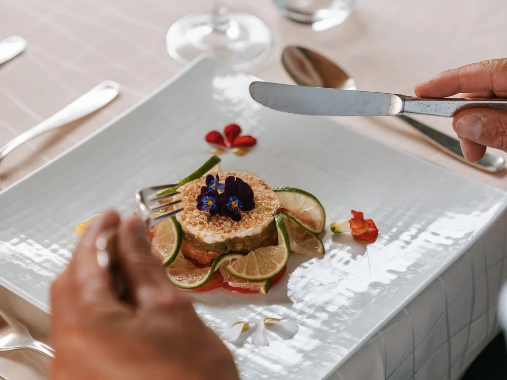 Gedeckter Tisch mit Gourmetgericht und Person, die Besteck hält