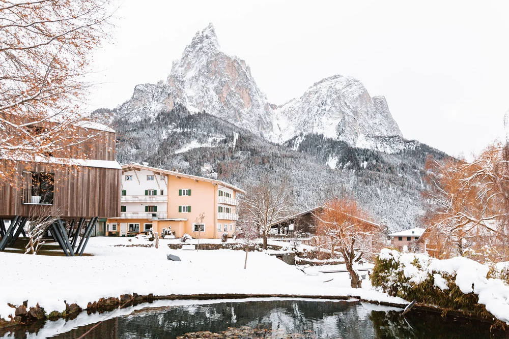 Schneebedeckte Berge und Häuser mit einem Teich im Vordergrund