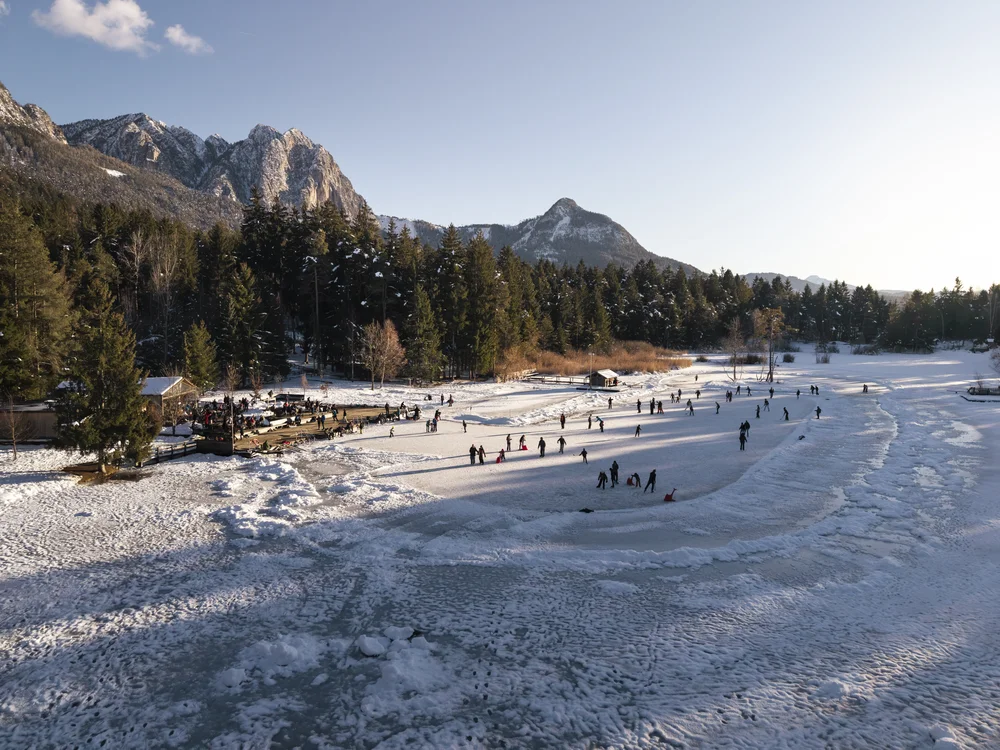 Menschen beim Schlittschuhlaufen auf zugefrorenem See vor Bergkulisse