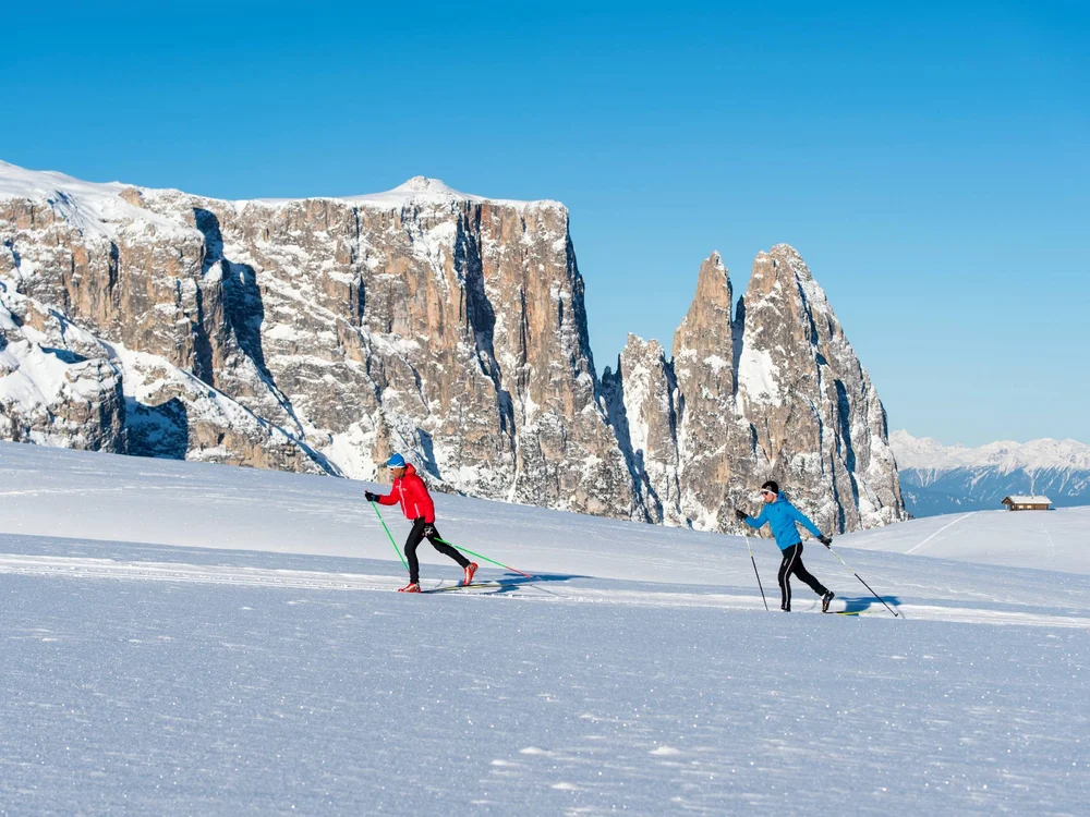 Zwei Langläufer vor schneebedeckten Bergen bei klarem Himmel