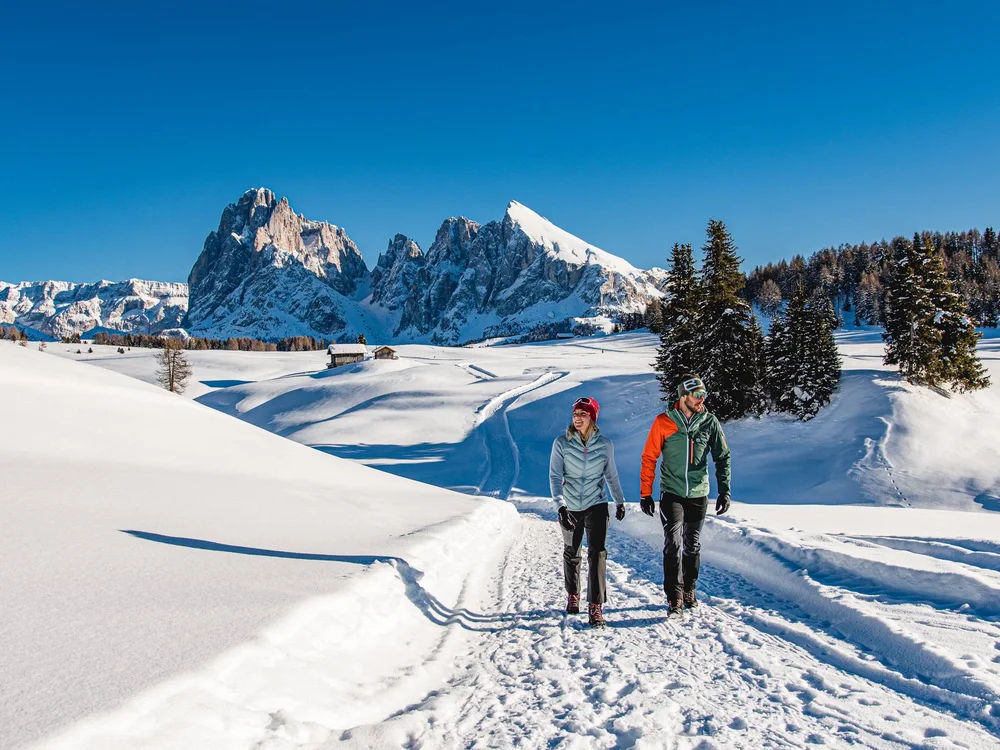 Paar wandert auf verschneitem Weg mit Bergpanorama im Hintergrund