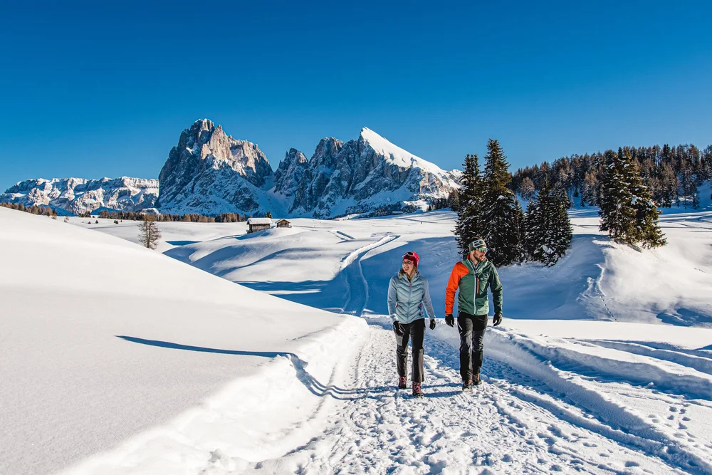 Paar wandert auf verschneitem Weg mit Bergpanorama im Hintergrund