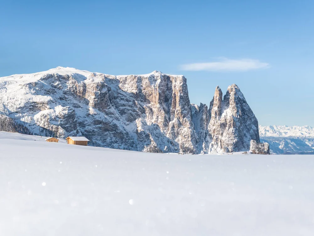 Schneebedeckte Berge mit zwei Holzhütten unter blauem Himmel