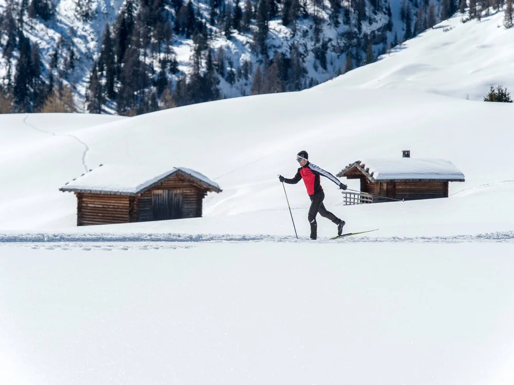 Langläufer in roter Jacke vor schneebedeckten Hütten und Bergen