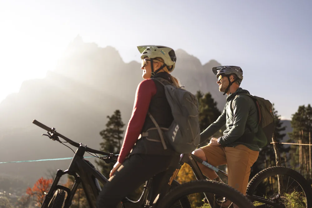 Zwei Radfahrer mit Helmen und Rucksäcken vor einer Berglandschaft