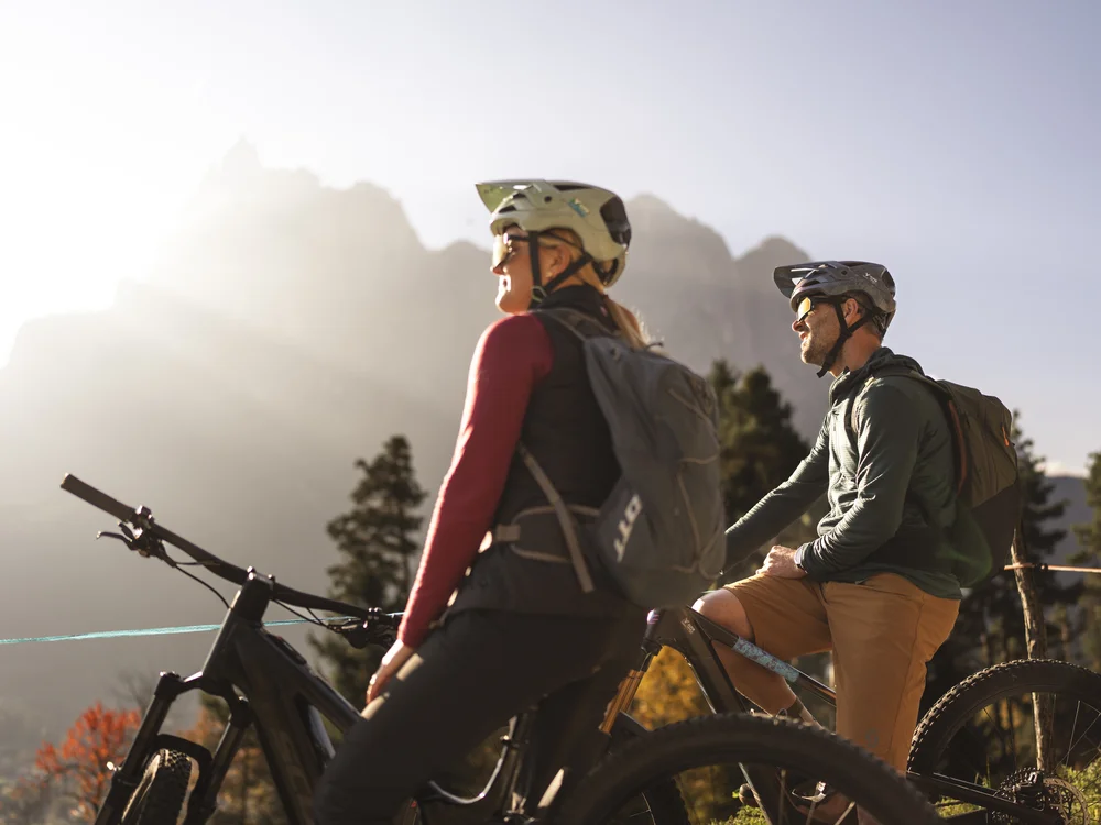 Zwei Radfahrer mit Helmen und Rucksäcken vor einer Berglandschaft