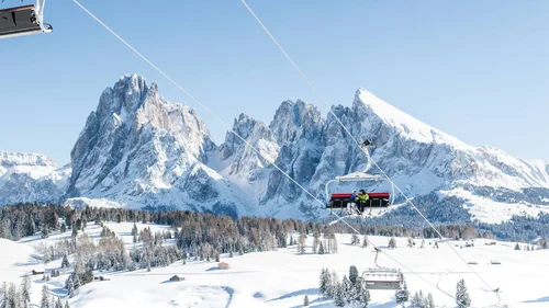 Skilift mit Fahrgästen vor schneebedeckten Bergen und blauem Himmel