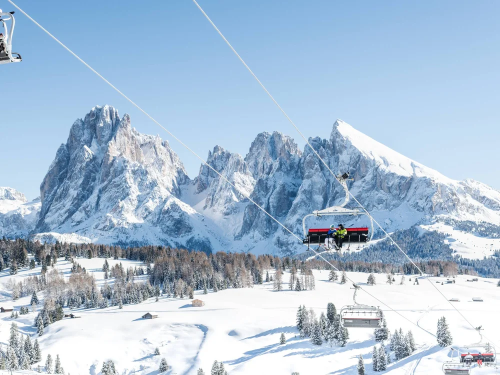 Skilift mit Fahrgästen vor schneebedeckten Bergen und blauem Himmel