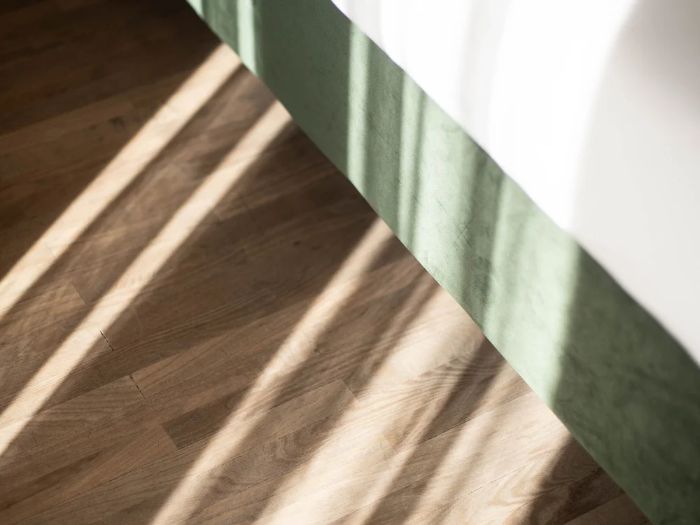 Sonnenlicht wirft Schatten auf Holzboden neben grünem Bett