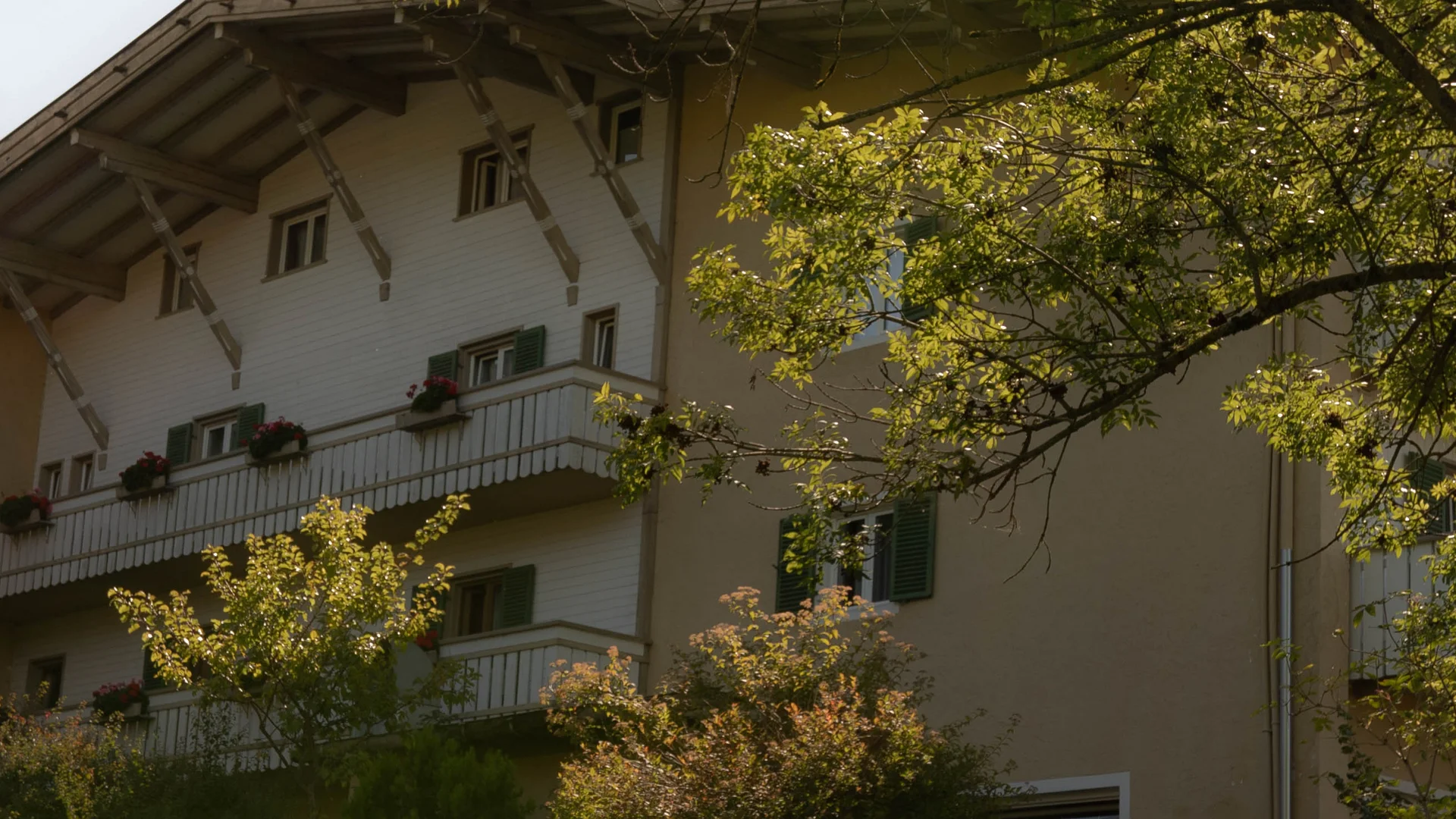 Haus mit Balkon und grünen Bäumen im Sonnenschein