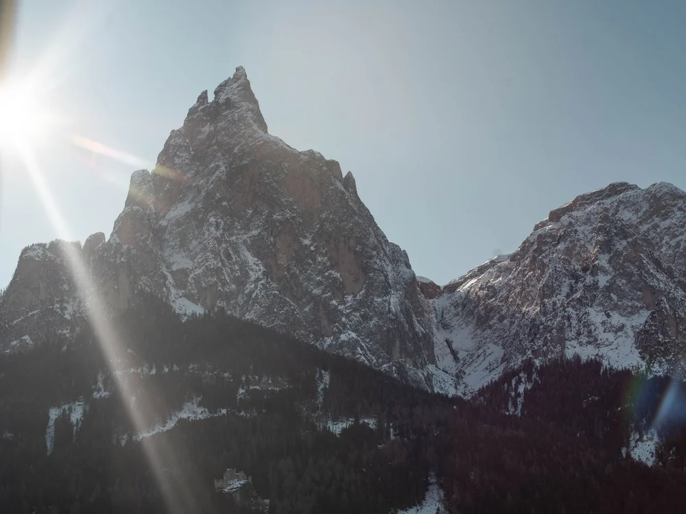 Sonnenschein über schneebedeckten Berggipfeln mit Wald im Vordergrund
