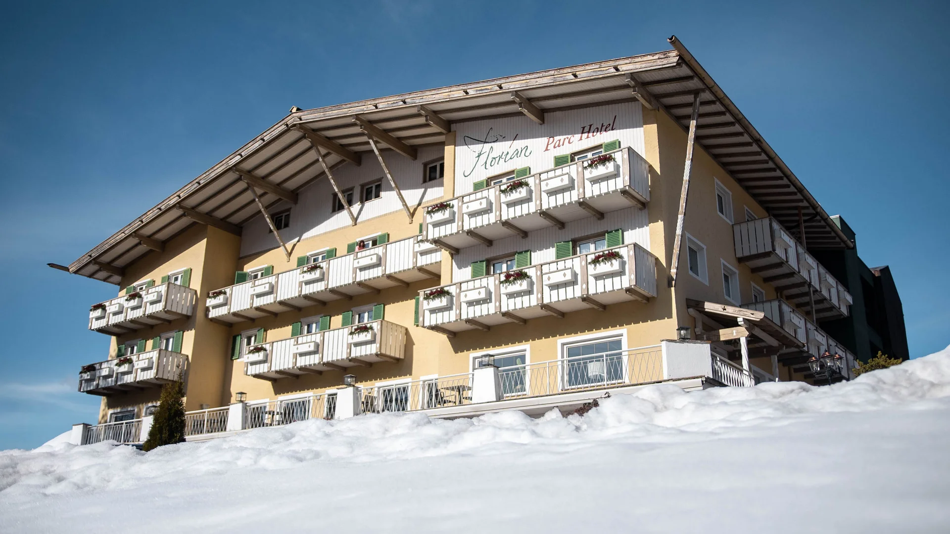 Hotel mit Balkonen und Schnee im Vordergrund unter blauem Himmel